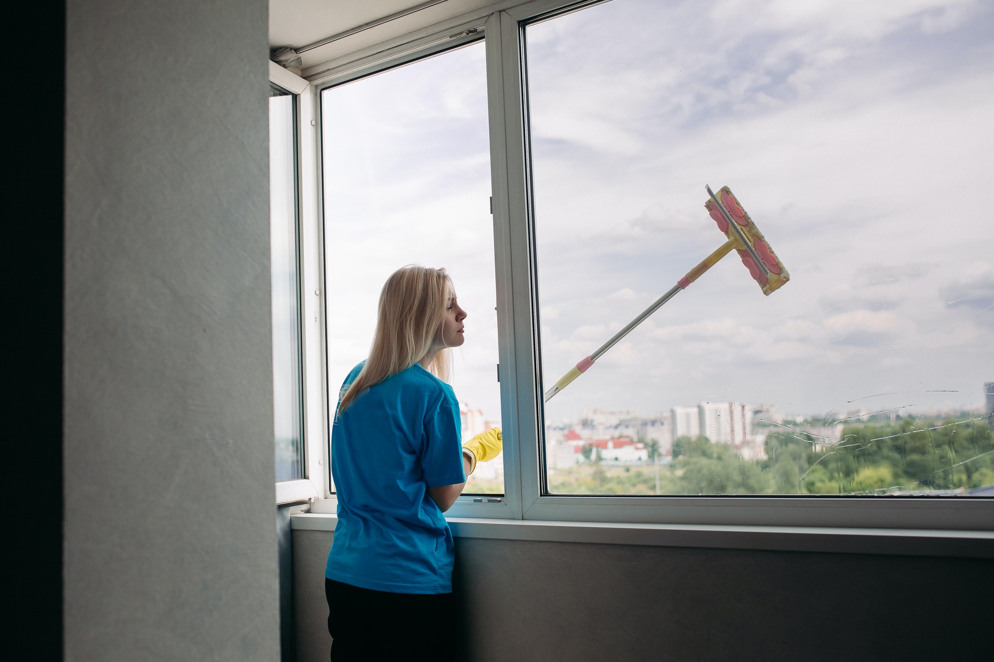 View of young blonde girl cleaning large open window