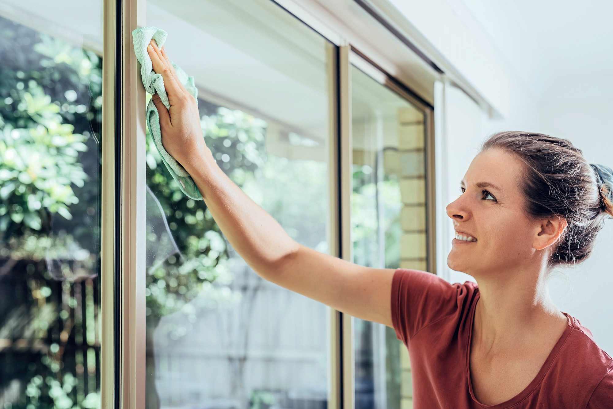 Young smiling woman is cleaning windows in a house, doing chores